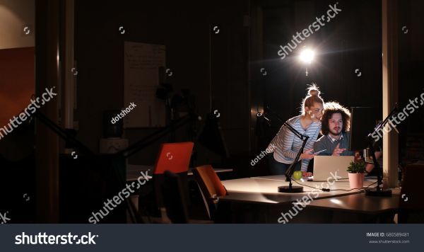 Two people working on a computer in a dimly lit room with a spotlight on them.