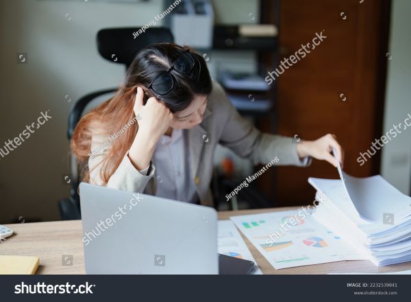 A disgruntled woman sifting through papers and checking through her laptop